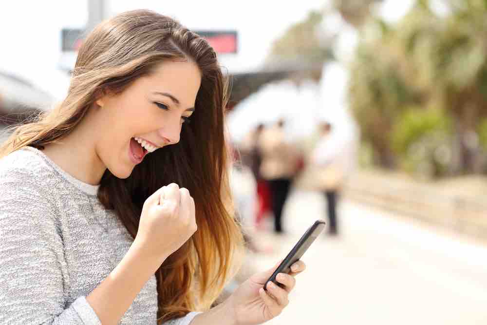 Euphoric,Woman,Watching,Her,Smart,Phone,In,A,Train,Station